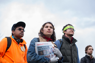 Students somberly listen to speakers at the rally. One student holds a newspaper related to socialism.